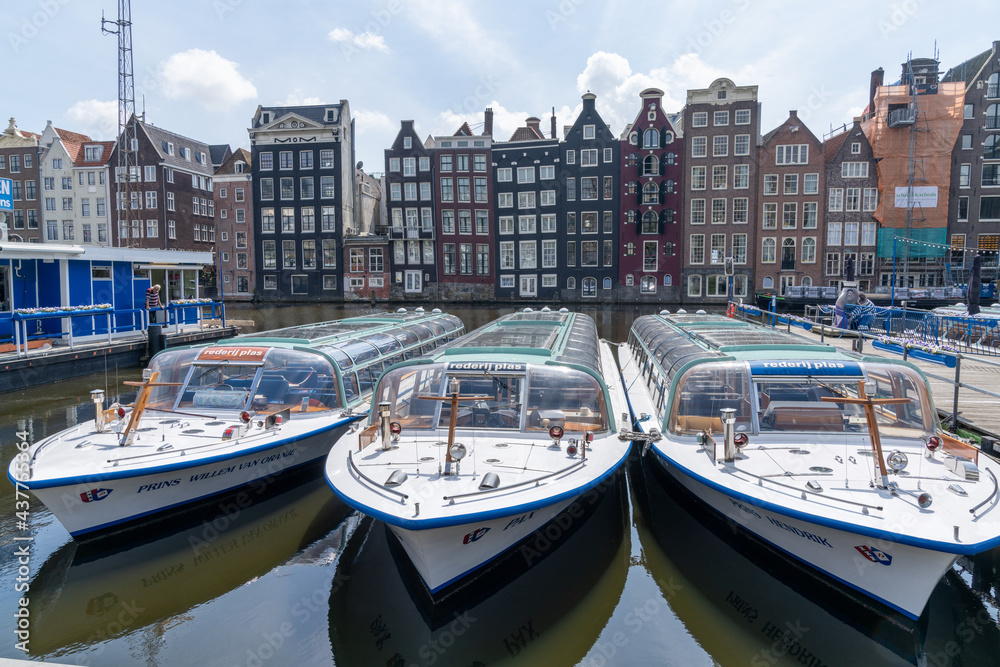 view of the iconic houses on the waterfront at the Damrak in downtown Amsterdam with city tour tourist boats in the foreground