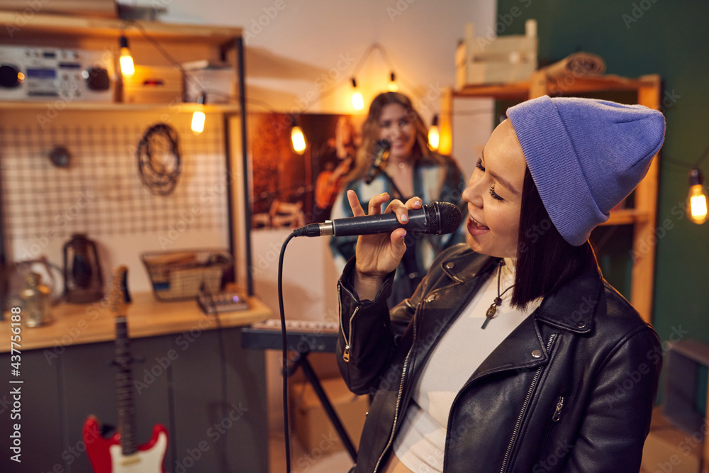 Cheerful young woman with microphone singing against her friend playing keyboard Cheerful young woman with microphone singing against her friend playing keyboard