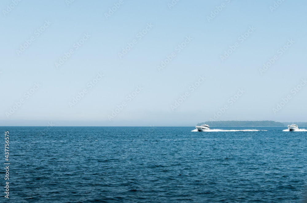 Landscape shot of a white motor boat moving fairly quickly on a blue ocean in Bruce Peninsula, Ontario, Canada.