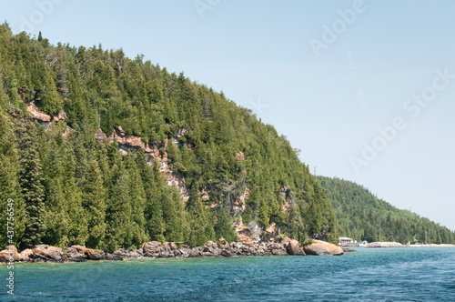 Landscape view of a very large hill of trees standing over an ocean/sea in Bruce Peninsula, Ontario, Canada.