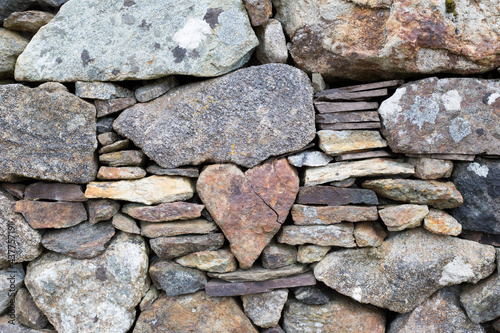 Heart-shaped stone stuck in the middle of a wall with other small and large stones photo