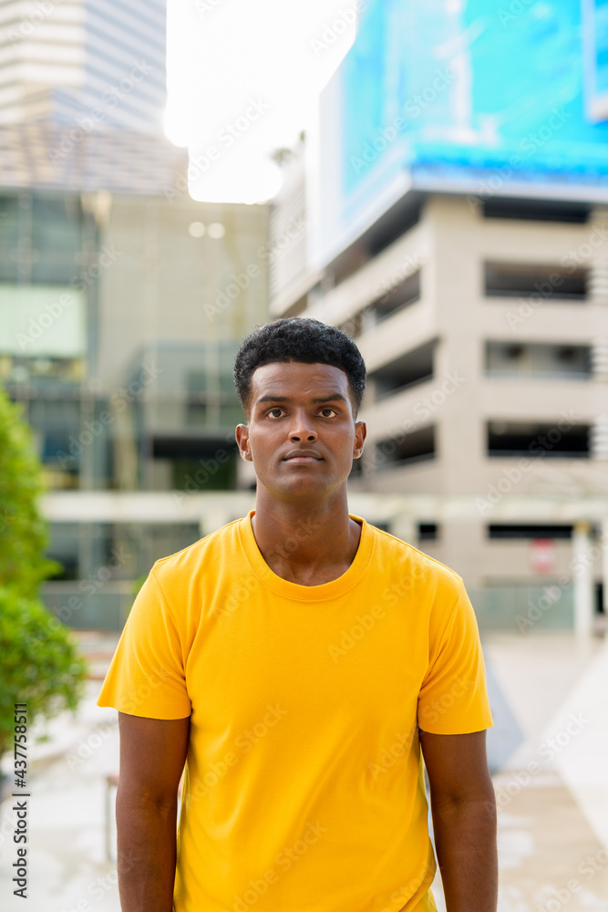 Vertical summer portrait of handsome black African man wearing yellow t-shirt outdoors in city Vertical summer portrait of handsome black African man wearing yellow t-shirt outdoors in city
