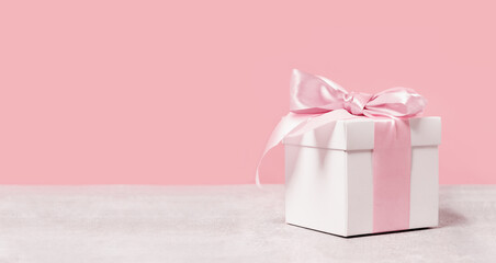 White gift box with shining pink ribbon bow on pink background. Gift or holiday concept. Mothers Day, birthday wedding or St Valentines day banner with copy space