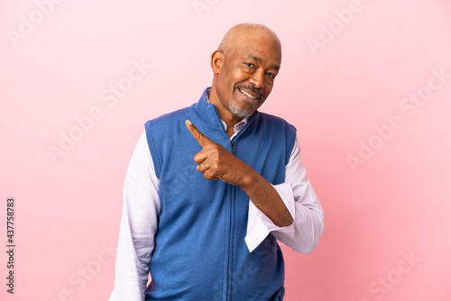 Cuban senior isolated on pink background pointing to the side to present a product © luismolinero