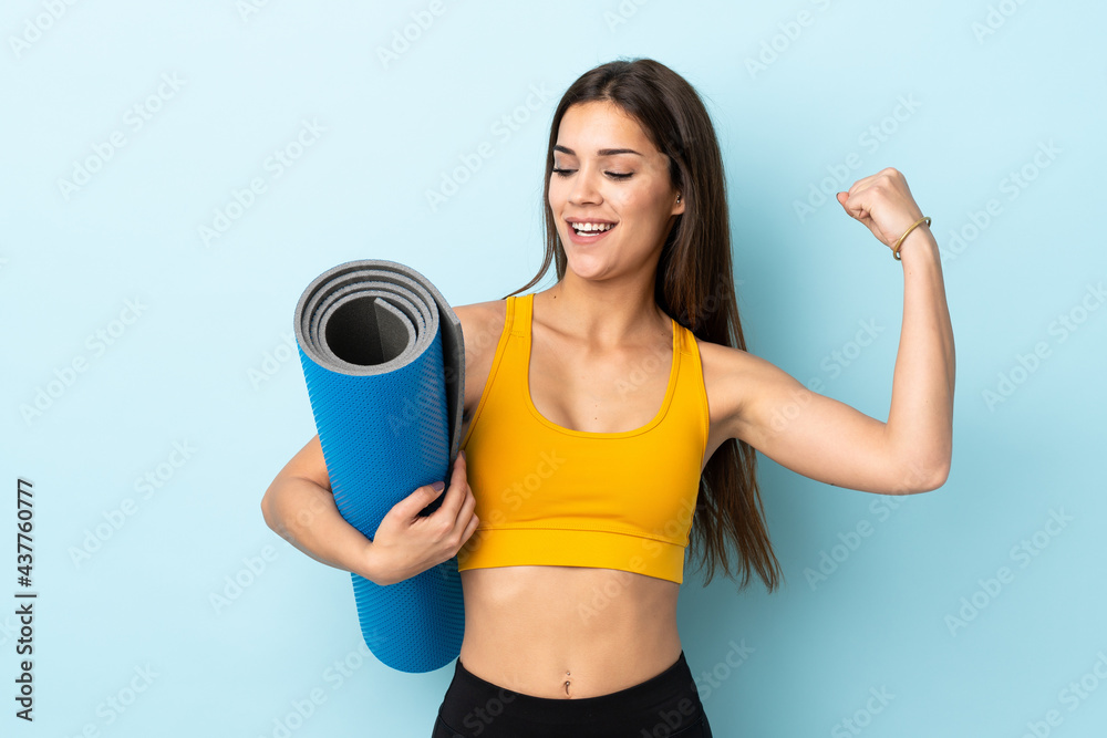 Young sport woman with mat isolated on blue background celebrating a victory