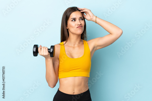 Young caucasian woman making weightlifting isolated on blue background having doubts and with confuse face expression © luismolinero