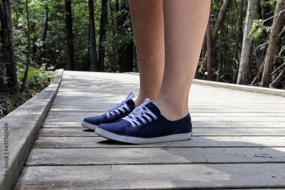 Close-up of a woman's legs in blue sneakers on a boardwalk footpath. Forest in the background. Brokenhead Wetland Trail.