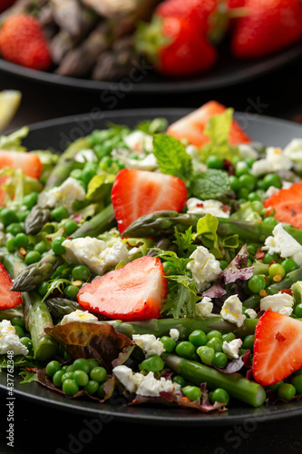 Asparagus and Strawberry Salad with vegetables, green peas and feta cheese in black plate. healthy food.