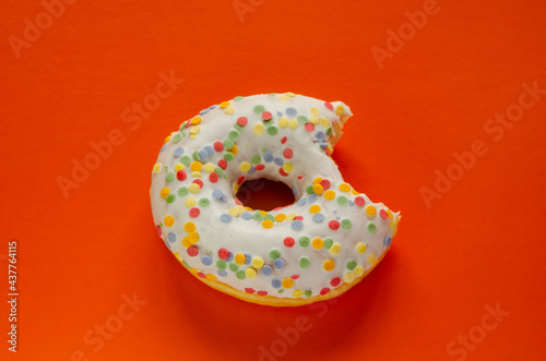 Donut in white glaze and round multi-colored balls on an orange background © ola_pisarenko