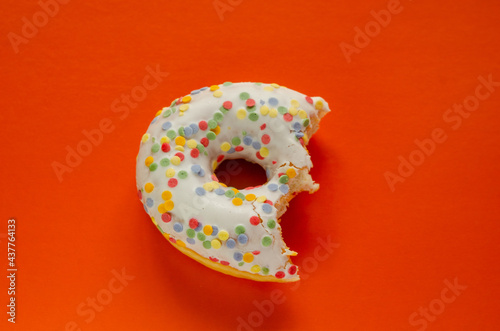 Donut in white glaze and round multi-colored balls on an orange background