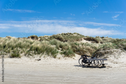 two bicycles parked in front of a large sand dune covered in grasses and reeds under a blue sky