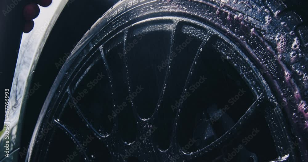 Car washing and detailing. Close up of cleansing wheels. Male hand spraying water and soap on wheel surface