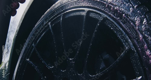 Car washing and detailing. Close up of cleansing wheels. Male hand spraying water and soap on wheel surface