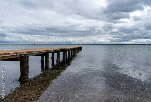 view of a long wooden pier leading out into clear ocean waters with sailboats behind © makasana photo