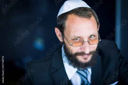 Bearded Charming Jewish man in white Yarmulke (hat, Kippah) looking with cunning eyes. Emotional expression. Sly bearded Jewish man smiling cunning looking at the camera. Selective focus on the eyes photo