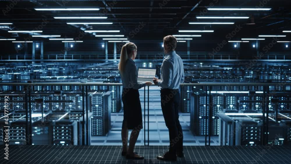 Data Center Male It Specialist and Female System administrator Talk, Use Laptop. Server Farm Cloud Computing Facility with Two Information Technology Professionals working on Cyber Secury. Static Wide Data Center Male It Specialist and Female System administrator Talk, Use Laptop. Server Farm Cloud Computing Facility with Two Information Technology Professionals working on Cyber Secury. Static Wide
