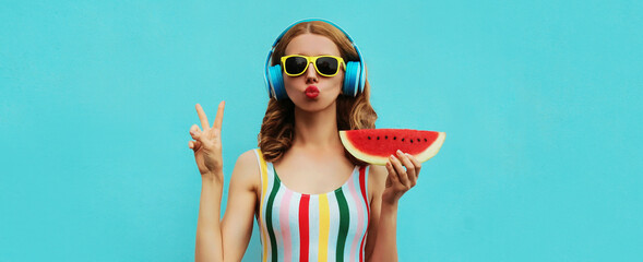 Summer fashion portrait of young woman in headphones listening to music with juicy slice of watermelon, female model blowing her lips posing on a colorful blue background