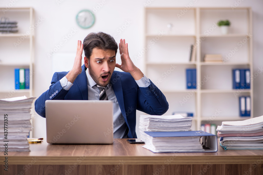Young male employee unhappy with excessive work in the office Young male employee unhappy with excessive work in the office