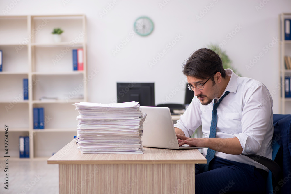 Young male employee unhappy with excessive work in the office Young male employee unhappy with excessive work in the office