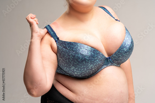 Large natural breasts in blue bra, biggest boobs on gray background photo