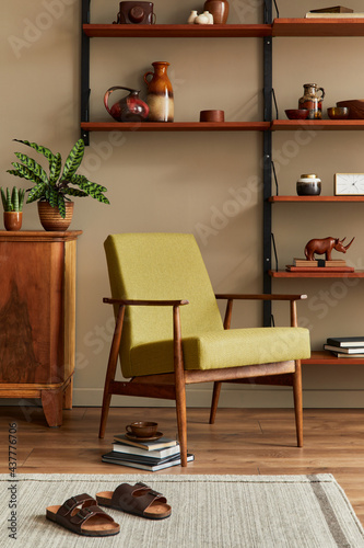 Stylish composition of retro living room interior with design armchair, wooden bookcase, coffee table, picture frames, plant, carpet, slippers, decoration and elegant accessories in home decor.  © FollowTheFlow