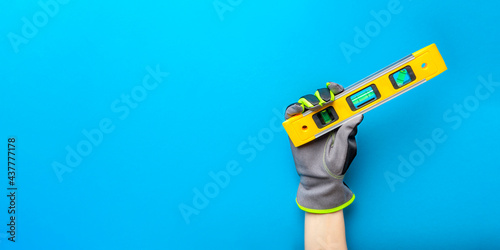 Building level. Hand in gloves holds a yellow building level on a blue background. Postcard or poster for print, place for text