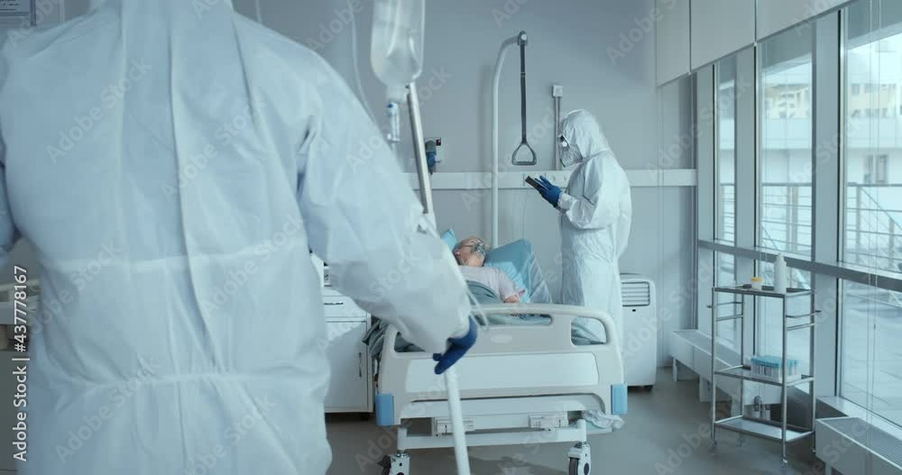 Doctor and nurse in ppe overall treating aged woman patient with covid-19 in hospital ward Doctor and nurse in ppe overall treating aged woman patient with covid-19 in hospital ward