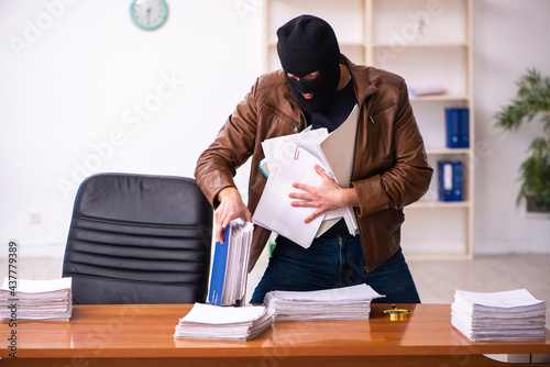 Bild auf Leinwand Young man in balaclava stealing information from the office
