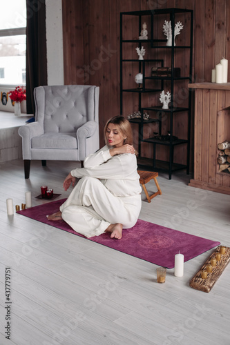 relaxed beautiful woman with fair hair in white clothes sits on the yoga mat and looks aside