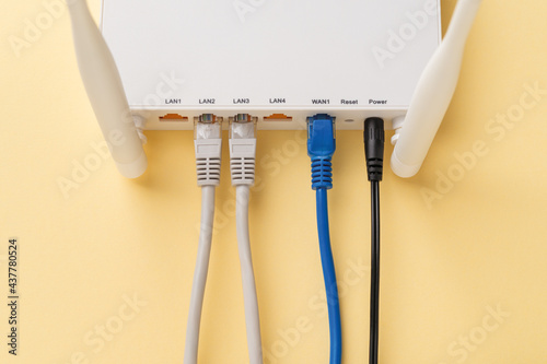 White Wi-Fi wireless router with connected network and power cables on a yellow background. Home and office wlan router with inserted internet cables. Internet hardware close-up. photo