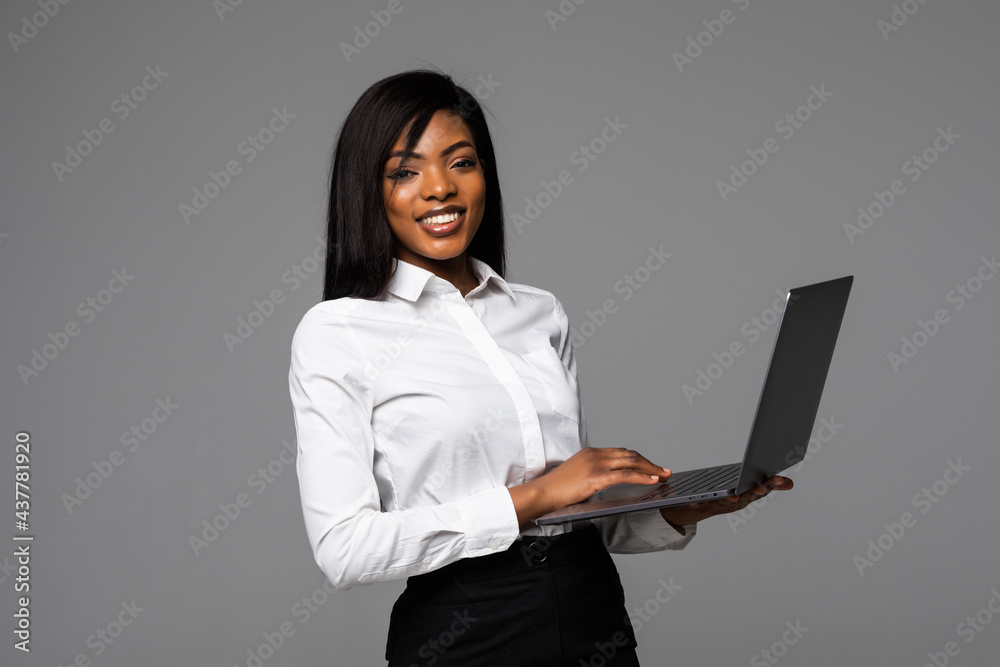 Photo of young african business woman standing over grey wall with laptop computer. Photo of young african business woman standing over grey wall with laptop computer.