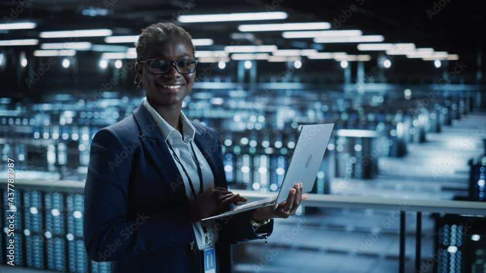 Data Center Female Programmer Using Laptop Computer, Smiling and Looking at Camera. In Cloud Computing Server Farm System Administrator Working on IT Maintenance for Iaas, saas, paas. Medium Shot Data Center Female Programmer Using Laptop Computer, Smiling and Looking at Camera. In Cloud Computing Server Farm System Administrator Working on IT Maintenance for Iaas, saas, paas. Medium Shot