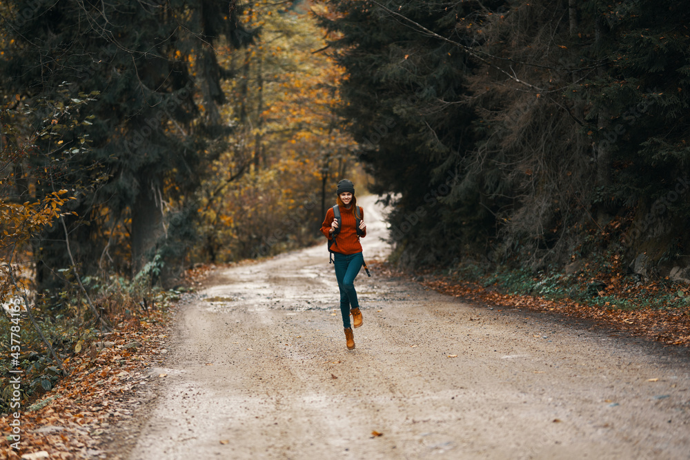 happy travel with a backpack in a warm sweater, trousers and boots walks along the road in the autumn forest happy travel with a backpack in a warm sweater, trousers and boots walks along the road in the autumn forest