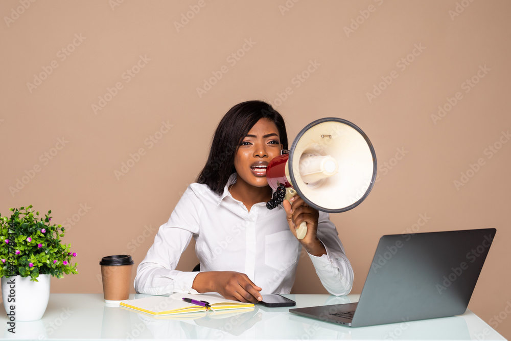 African businesswoman sitting at the table and shouting in megaphone on laptop African businesswoman sitting at the table and shouting in megaphone on laptop