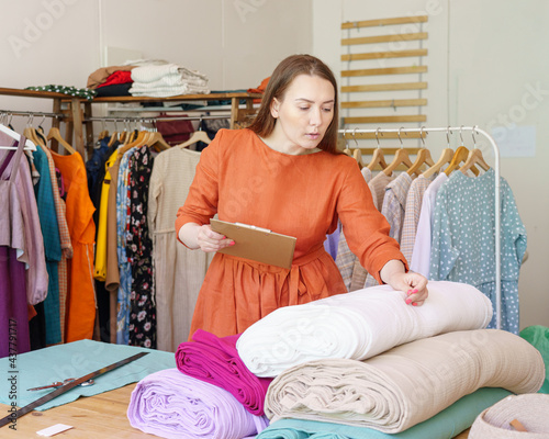 Fashion business. Busy young woman fashion designer dressmaker checking rolls of fabric in workshop before sewing new fashionable dress collection. Female seamstress working at her workshop or studio photo