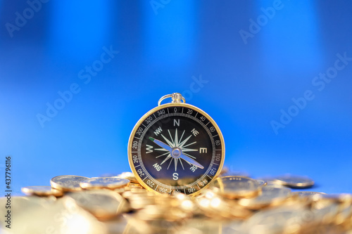 Business, Money Direction and Planning Concept. Closeup of vintage compass on pile of gold coins with blue background.