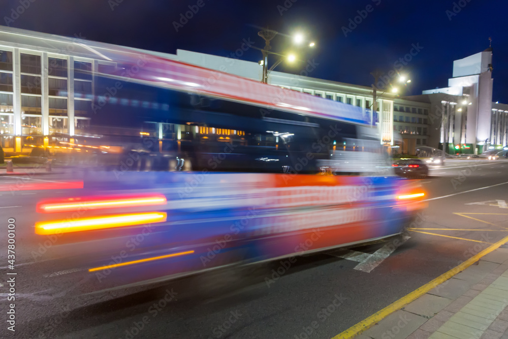 The movement of a blurred minibus along the avenue in the evening.