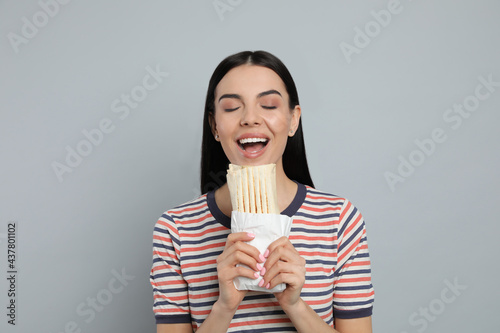 Young woman eating delicious shawarma on grey background