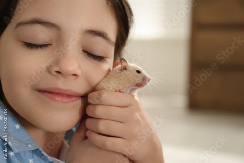 Little girl hugging cute hamster at home, closeup