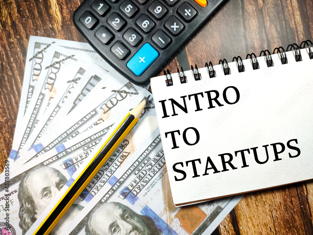 Fototapeta premium Business concept.Text Intro to startups with banknote,pencil and calculator on wooden table background.