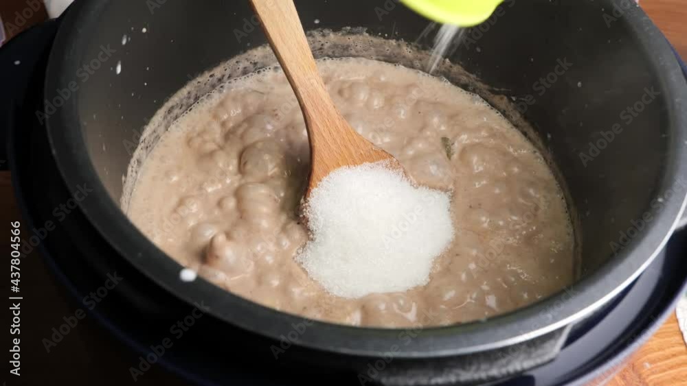 Adding sugar into green bean porridge or bubur kacang hijau in a boiling pot and stir with a wooden spoon.