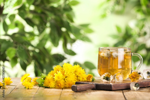 Delicious fresh tea, dandelion flowers and ice cubes on wooden table against blurred background. Space for text