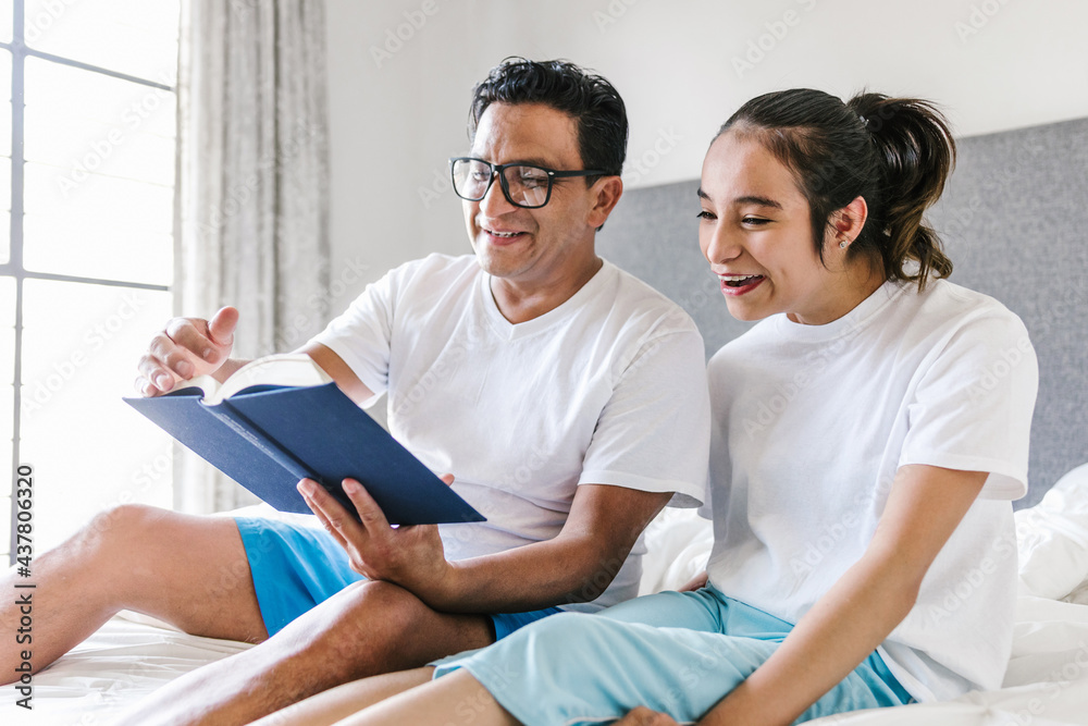 Obraz premium mexican girl with cerebral palsy reading a book with her father on bed at Home in disability concept in Latin America