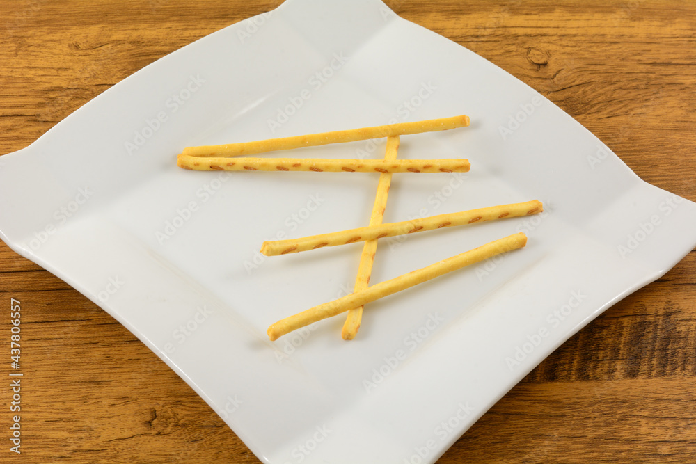 Buttered corn flavored pretzel sticks on white snack plate on table