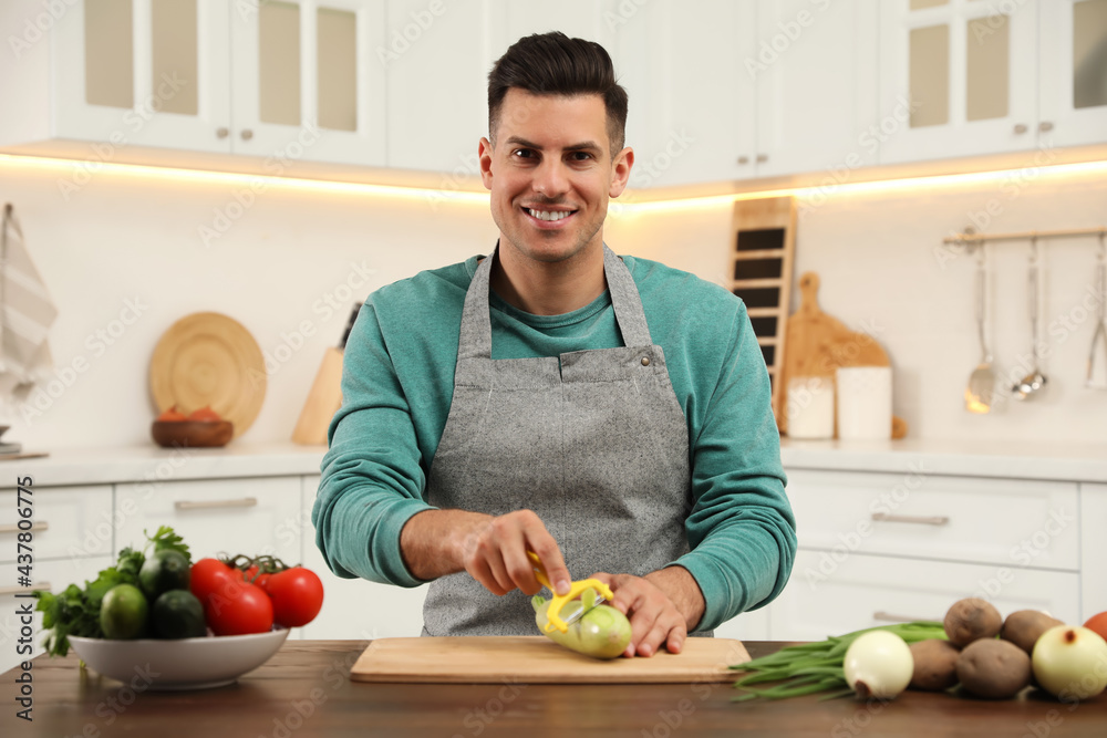 Fototapeta premium Man peeling zucchini at table in kitchen. Preparing vegetable
