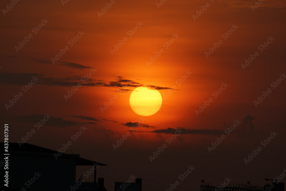 Fototapeta premium Yellow Sun rising in Orange sky with clouds in between