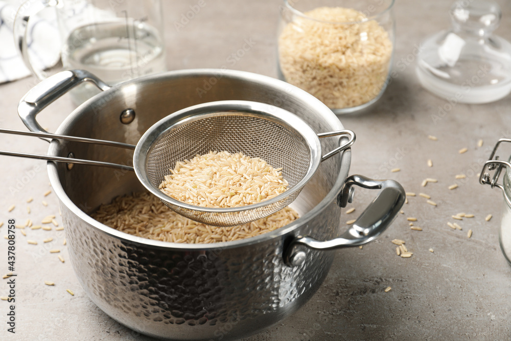 Sieve with rice in pot on grey table