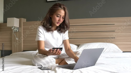 Beautiful Asian women on the bed with laptop and credit card, she shopping online, Pay utility bills, buy ticket in the morning. Morning relax time for shopping online