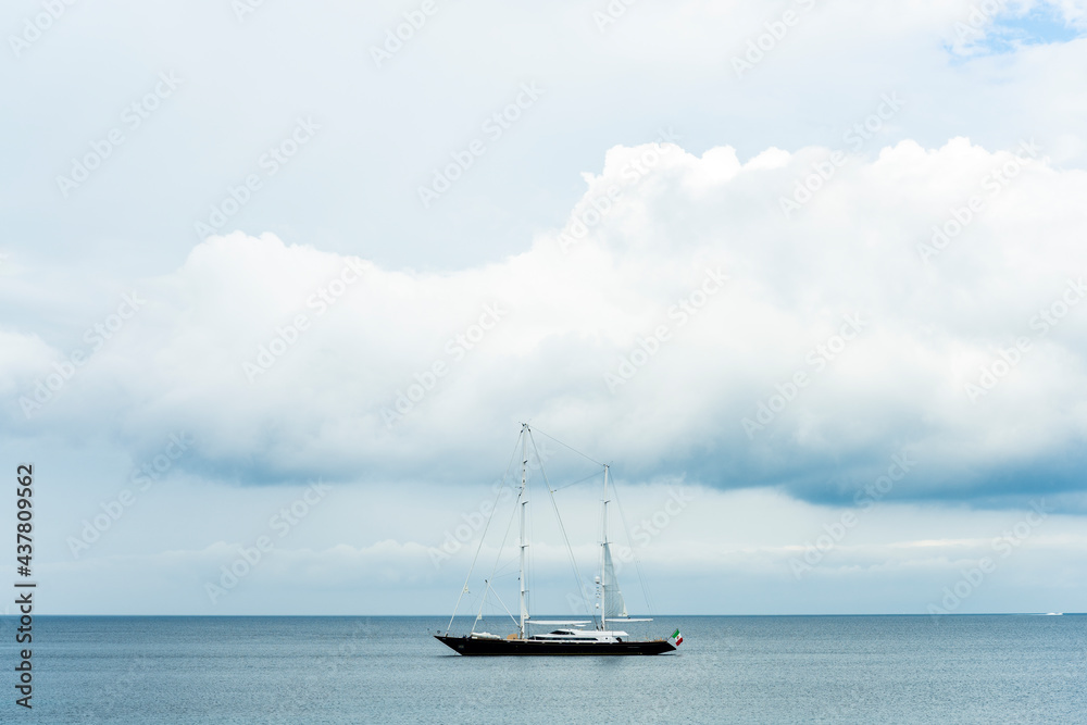 Fototapeta premium Stunning view of a luxury sailboat sailing on a beautiful calm sea during a dramatic, cloudy day.Sardinia, Italy. Recreational pursuit, copy space.