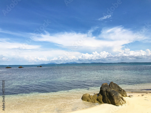 Beautiful seascape summer background. A lonely rock on the sand beach on the sea, cloud and blue sky background on a sunny day.